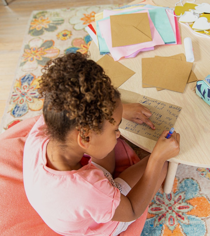 Young girl sitting at the table in her house making a kids thank you card