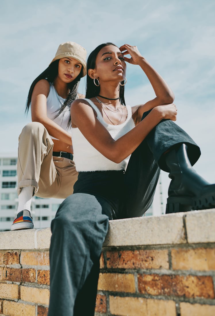 two women perch on a brick wall and pose for a photo as they consider how they'll be the least affec...
