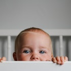 Portrait of a baby peeking over the bars of her crib.