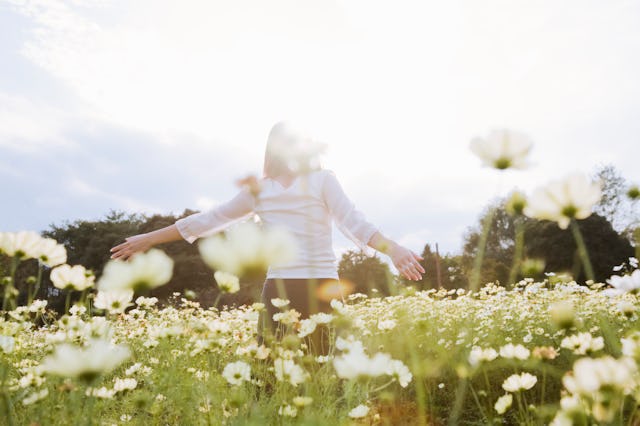 a woman walking on the flower field with spreading her hands out, the 2023 horoscope for leo says it...