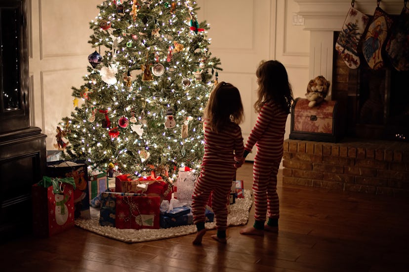 Rear view of preschool girls holding hands looking at lit, decorated Christmas tree, in a story abou...