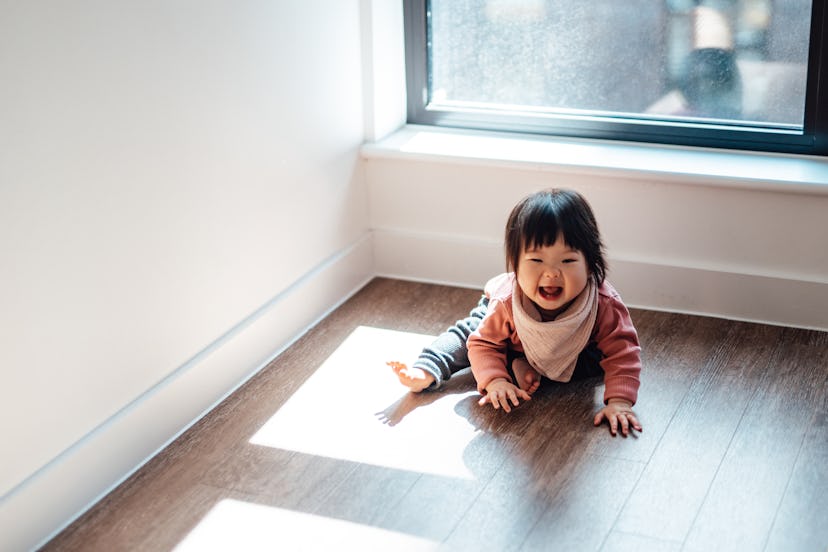 Smiling baby girl sitting on the wooden floor at home in the sunlight, in an article about new year ...