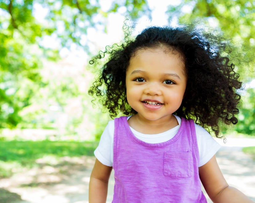 Cute African American little girl walks in the park on a sunny day. The wind is blowing her curly bl...