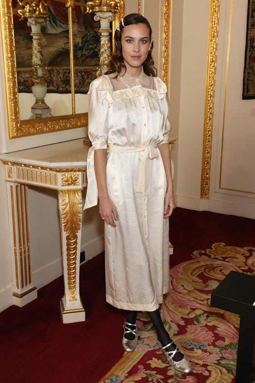 Alexa Chung attends the Simone Rocha show wearing a white silk dress and silver Mary Janes. 