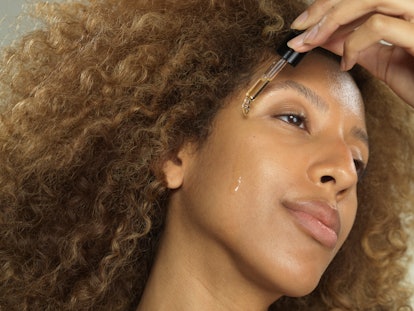 A Black woman applying a skin care serum to her face. 