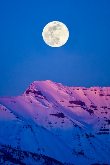 A full moon over a snowy mountaintop.
