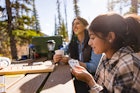 快乐的母亲和女儿在阳光明媚的露营地野餐桌上玩克里比奇万博体育app安卓版下载
