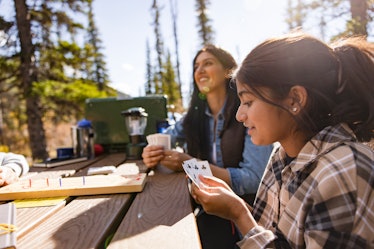 Happy mother and daughter playing cribbage at sunny campsite picnic table