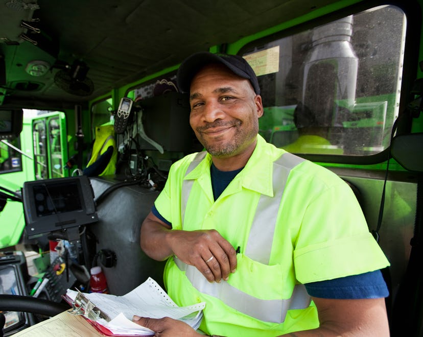 Gifts for garbage collectors, like this smiling sanitation worker sitting in driver's seat of trash ...