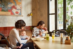 Happy mother with their babies sitting at table in restaurant When It's Safe To Bring Your Newborn T...