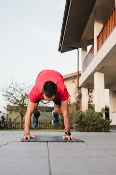 A man doing burpees outside on a yoga mat.