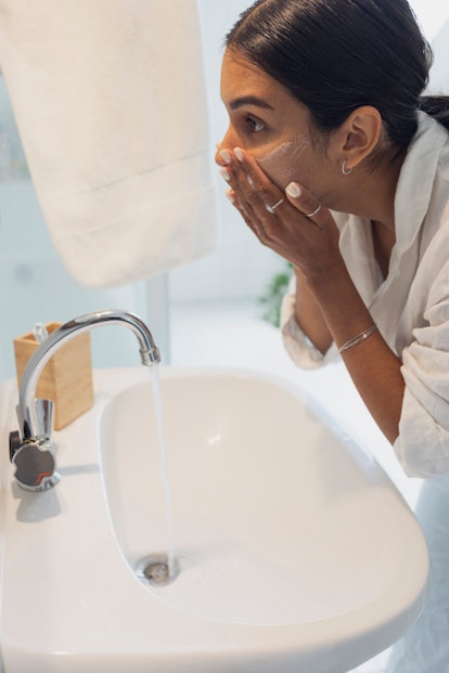 Woman in white pajamas washing face at home.