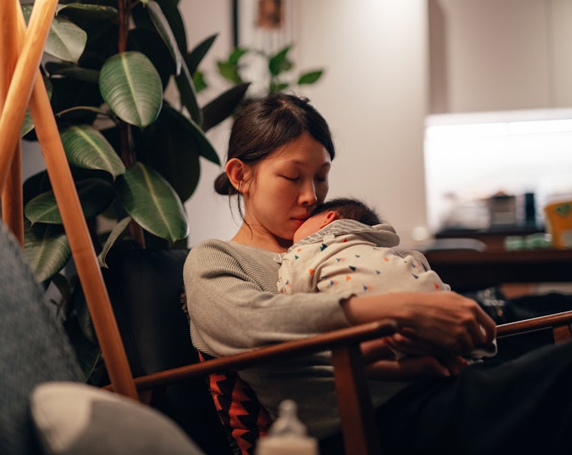 Tired mom holding her baby in an article about baby sleeps well at night but not for naps