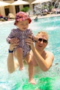 Adorable smiling beautiful baby girl swims and plays with father in the swimming pool by the sea. Th...