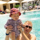 Adorable smiling beautiful baby girl swims and plays with father in the swimming pool by the sea. Th...