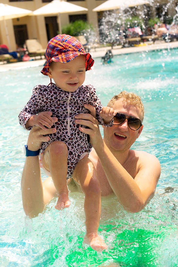 Adorable smiling beautiful baby girl swims and plays with father in the swimming pool by the sea. Th...