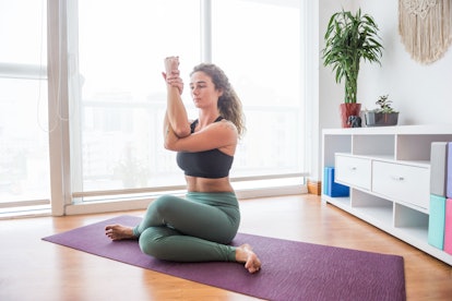 A woman does a seated eagle pose, which is part of a quick yoga workout at home. 