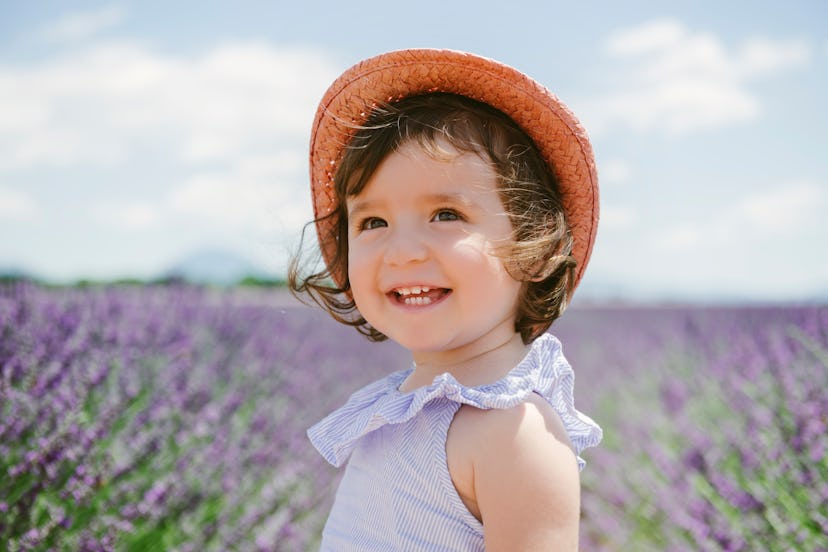 Toddler girl wearing straw hat in a lavender field, in a story about baby name trends for 2023.