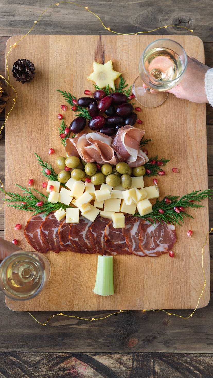 Cheese and charcuterie board in the shape of a Christmas tree. Two people eating. Copy space. Top vi...