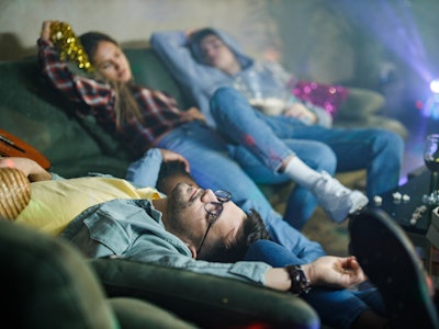 Group of wasted friends sleeping after party in the living room. Focus is on man in the foreground.