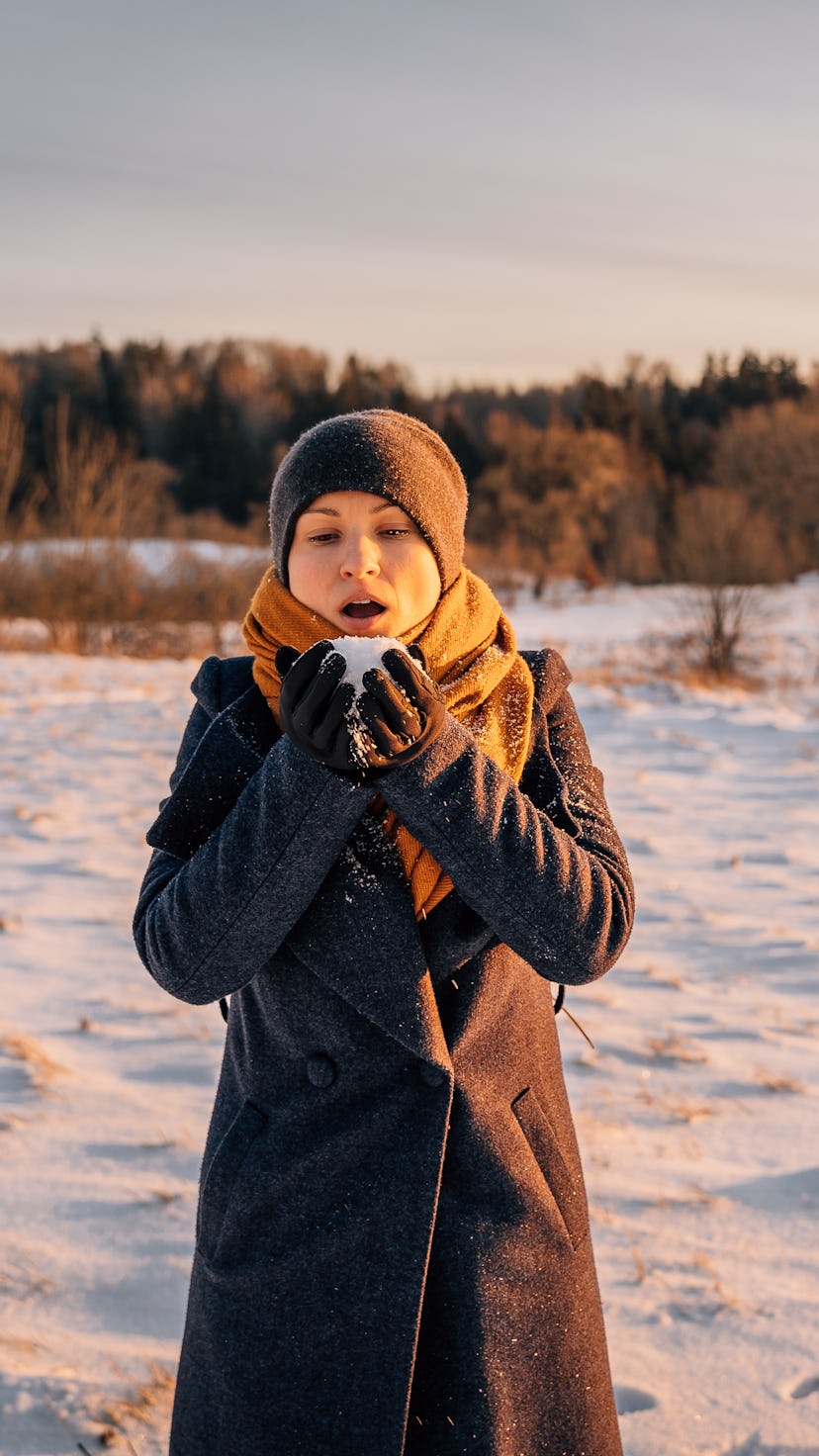A woman in winter with a handful of snow in her palms prepared to blow it away.
