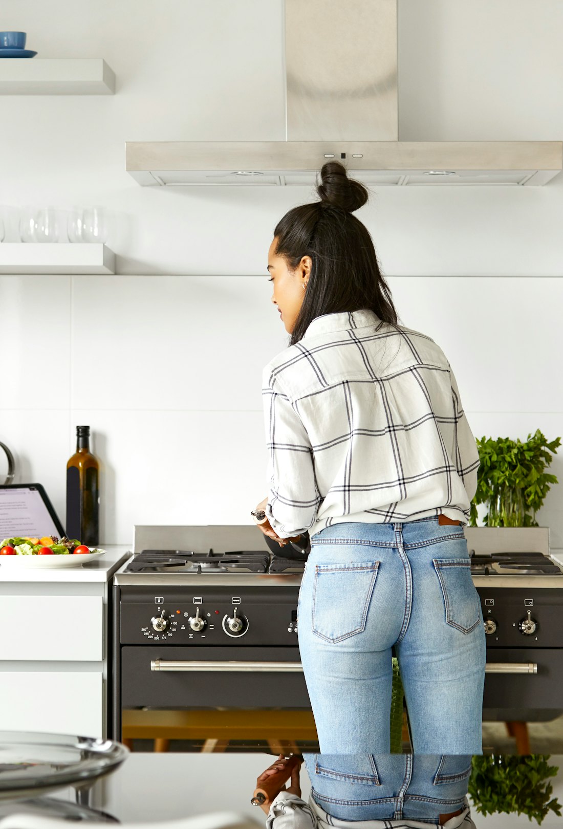 Rear view of woman looking at digital tablet while cooking food in a kitchen at home, searching the ...