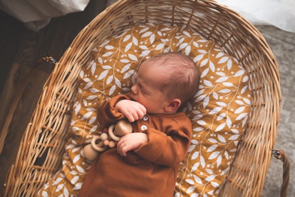 刚出生的婴儿穿着时尚的棉质工作服睡在自然的柳条篮子里。