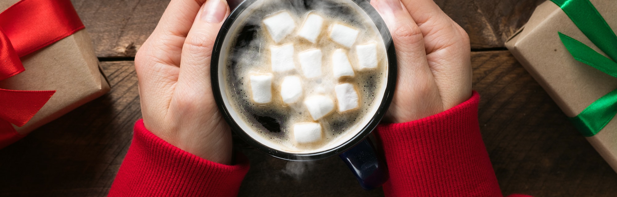 A girl or a woman in a red sweater holding in his hand a warming mug of hot coffee with marshmallows...