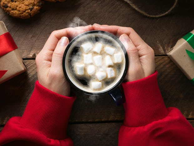 A girl or a woman in a red sweater holding in his hand a warming mug of hot coffee with marshmallows...