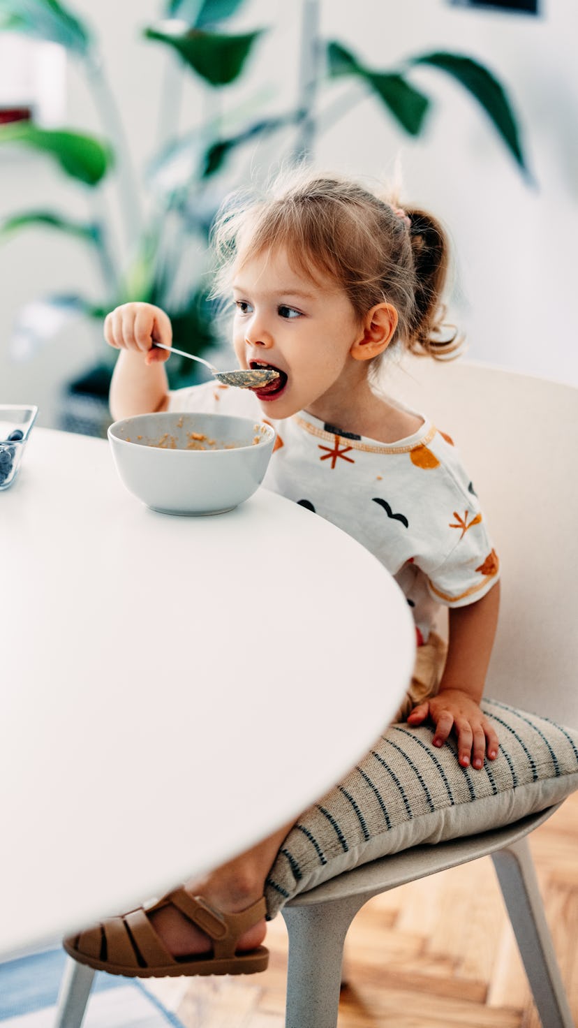 Cute girl having fun while eating cereals with fruit for breakfast in the kitchen.