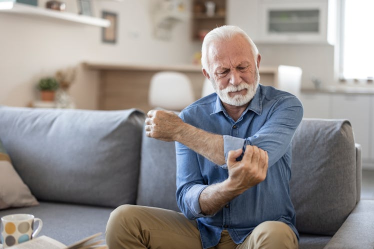 Senior man with arm pain.Old male massaging painful hand indoors. Old man hand holding his elbow suf...
