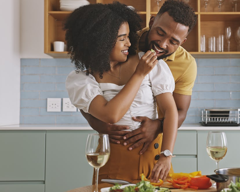 A couple cooking together and feeding one another while touching, an example of romantic gestures fo...