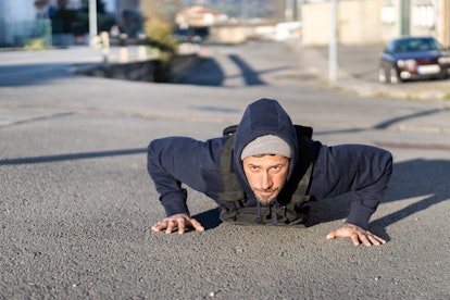 man with tattoos and winter hat doing push-ups on a sunny winter day with gym crosstraining weighted...