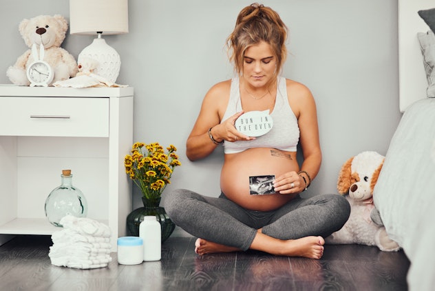 Full length shot of an attractive young pregnant woman sitting down and holding a picture of her son...