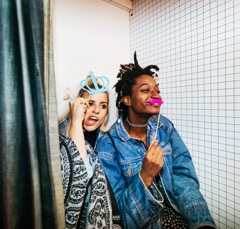 two friends take silly photos in a photobooth as they consider their january 2, 2023 weekly horoscop...