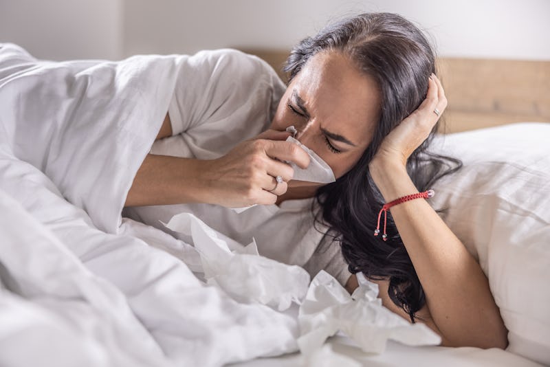 A sick woman sneezes into a napkin, lies in bed, has the flu or a cold.