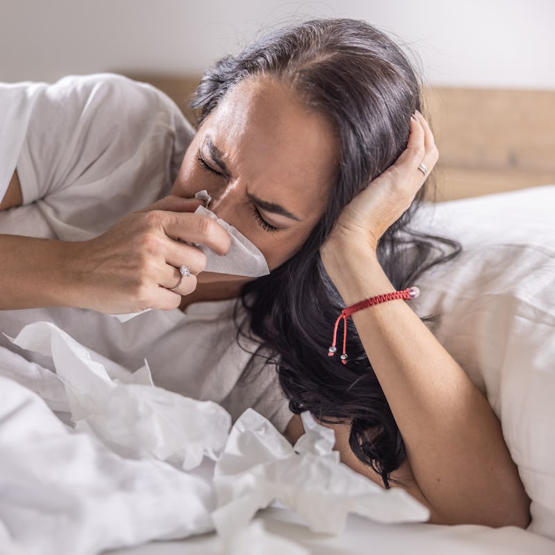 A sick woman sneezes into a napkin, lies in bed, has the flu or a cold.