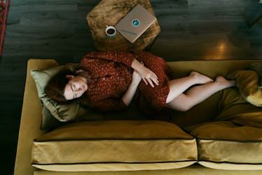 Portrait of a long-haired red-haired woman lying down on the sofa with cup of tea, crossed arms on s...
