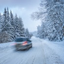 Driving a car in a remote snowy winter road through a pine forest