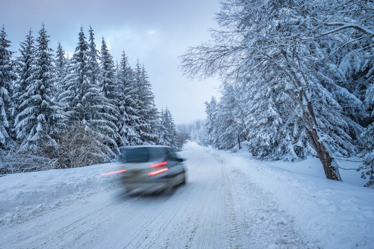 Driving a car in a remote snowy winter road through a pine forest