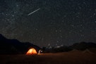 一颗流星在天空中，一个人在山附近的帐篷里露营。