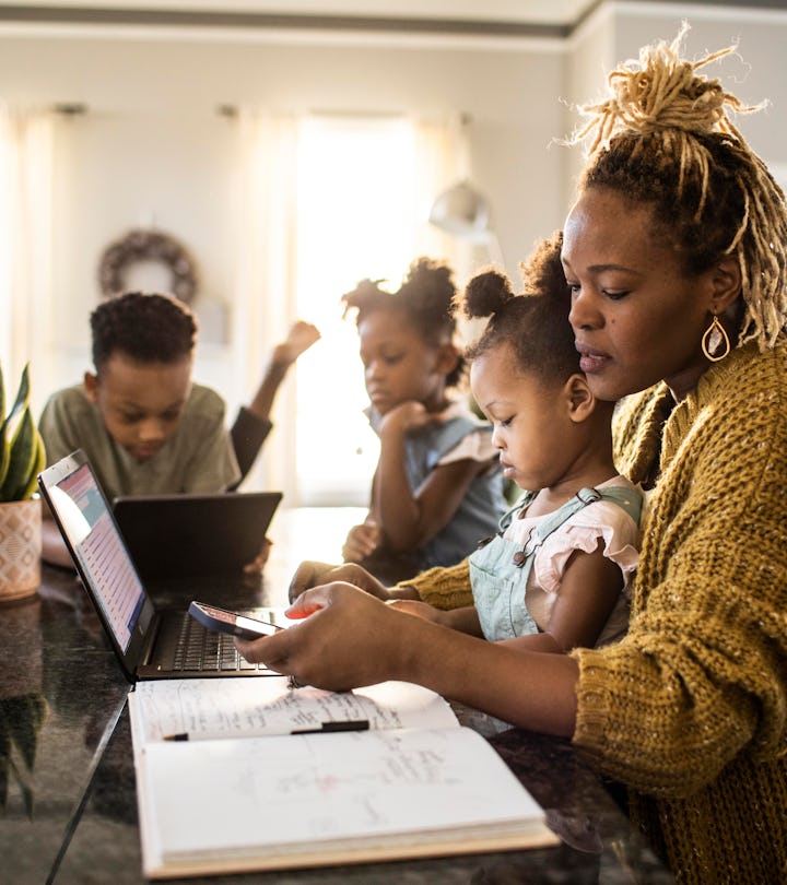 Mother working from home while holding toddler, family in background, like how a Libra prioritizes w...