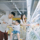 Young Chinese American family buying fresh vegetables in supermarket refrigerated section.