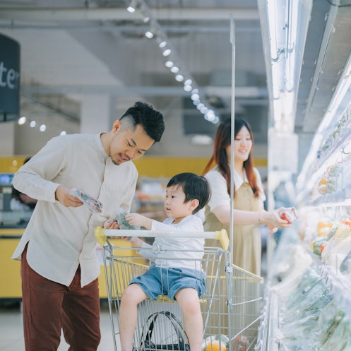 年轻的美籍华人家庭在超市冷藏区购买新鲜蔬菜。