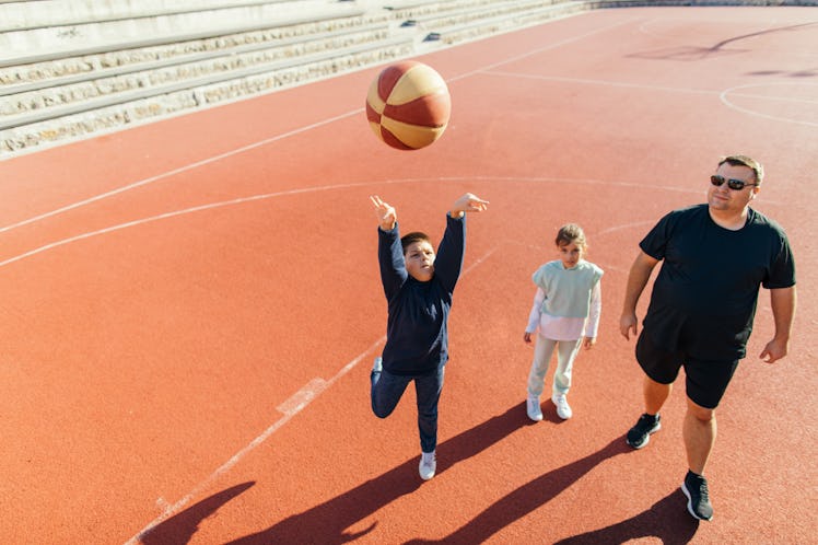 Boy with his father and sister on the basketball court learning how to shoot a basketball the right ...