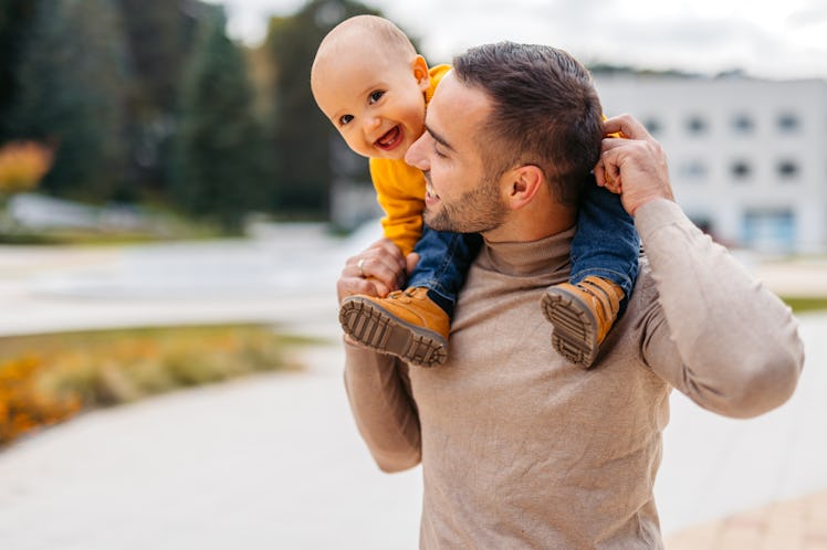 Young father playing with his toddler in the park in autumn. Holding him on his shoulders.