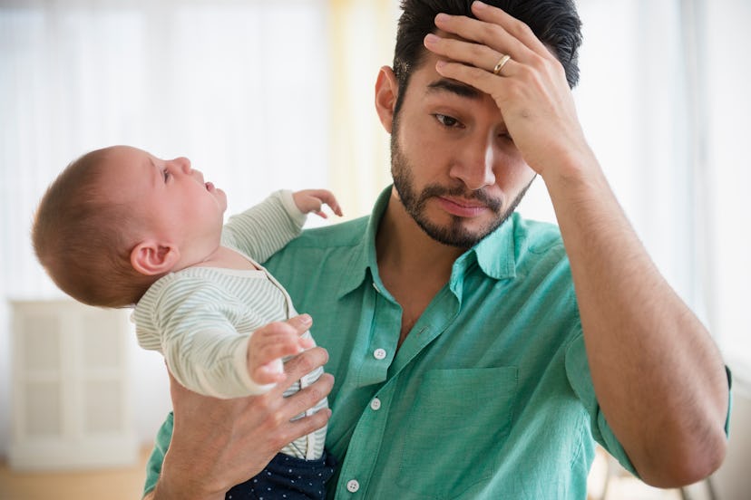 A baby throws its head back as a father looks frustrated.