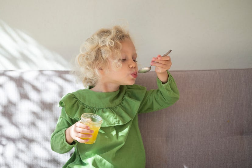 Girl eats honey with the spoon in an article about honey for toddler cough honey for kids cough