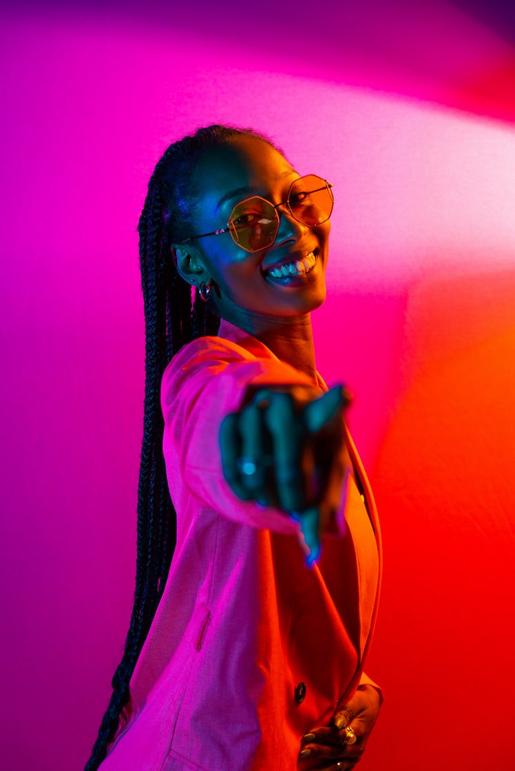 young woman smiles and points towards the camera as she considers her december 19, 2022 weekly horos...