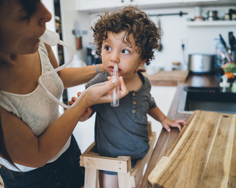 Mother using nasal aspirator for her son at home in the kitchen, what to do if baby's nose bleeds af...